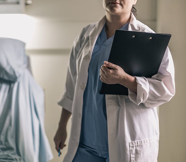 doctor in scrubs and lab coat holds a clipboard