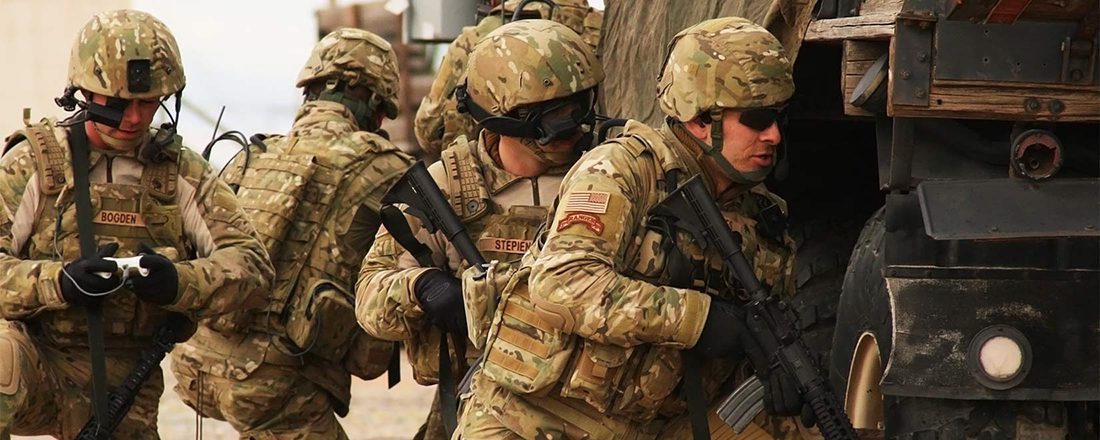 armed soldiers in uniform hide behind a large truck