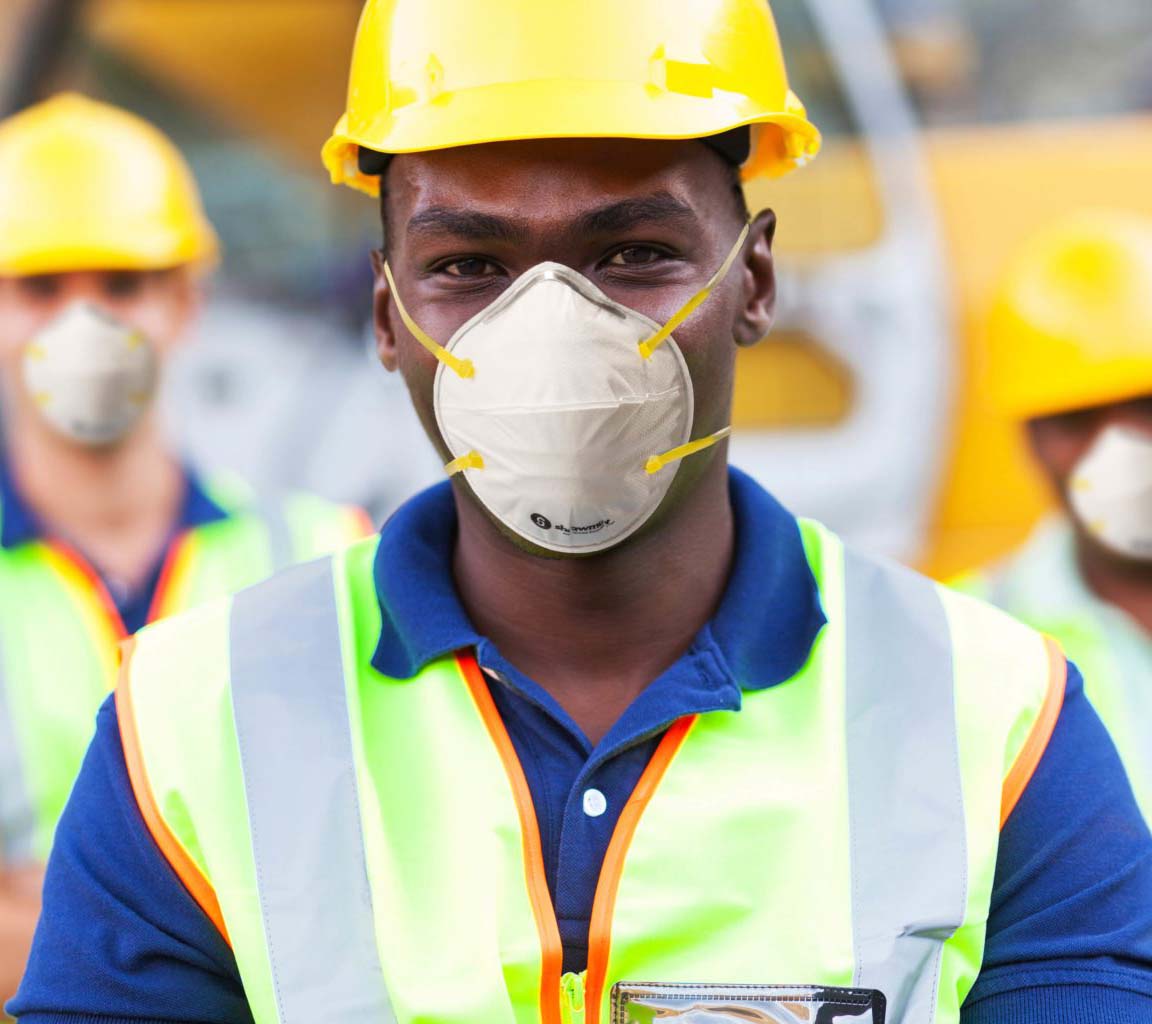a man in a yellow hard hat, reflective vest, and N95 mask