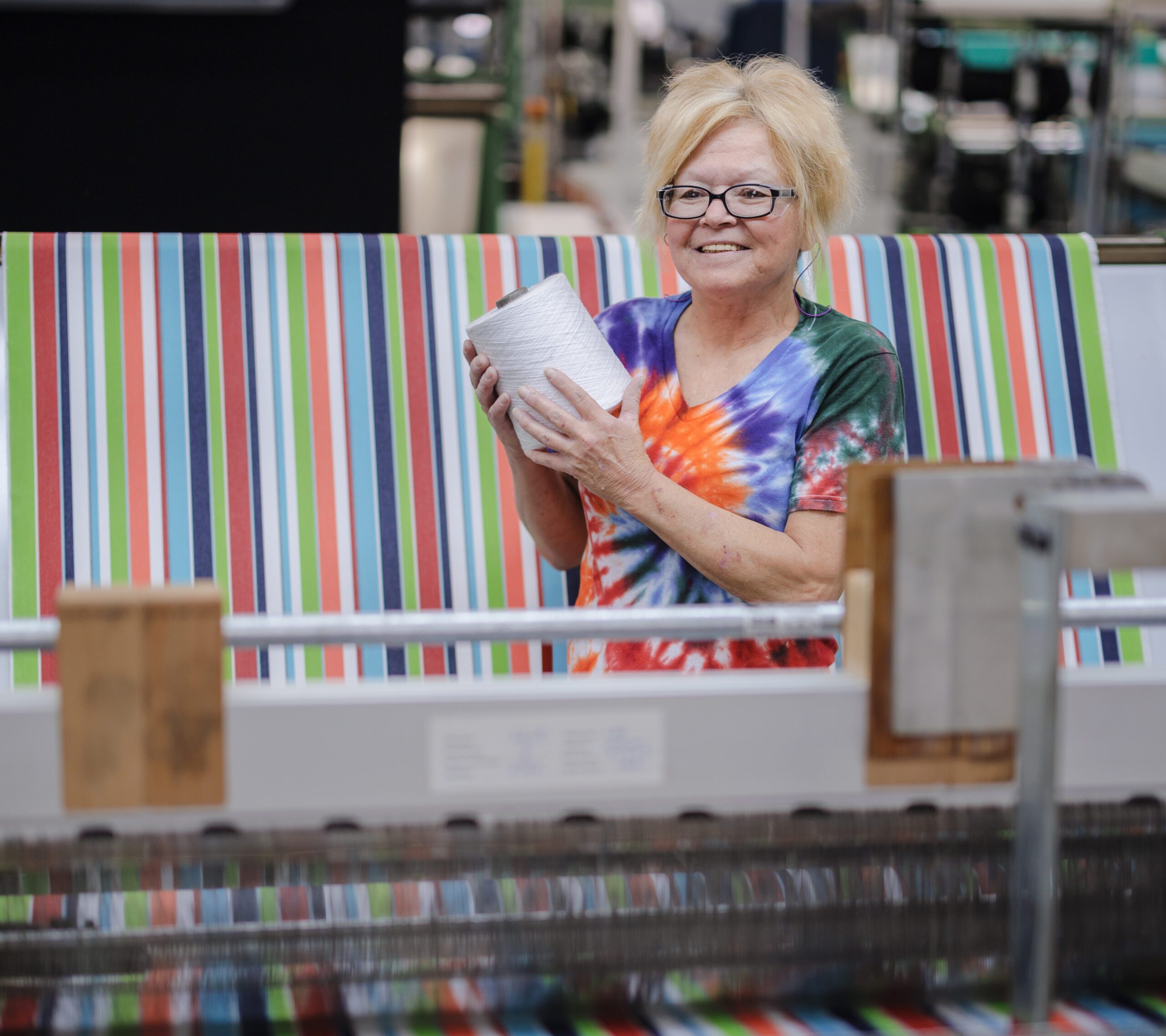 a woman poses in front of a loom with a spool of thread