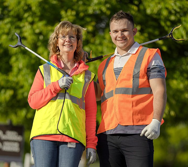 a man and woman in reflective vests smile and hold trash grabbers