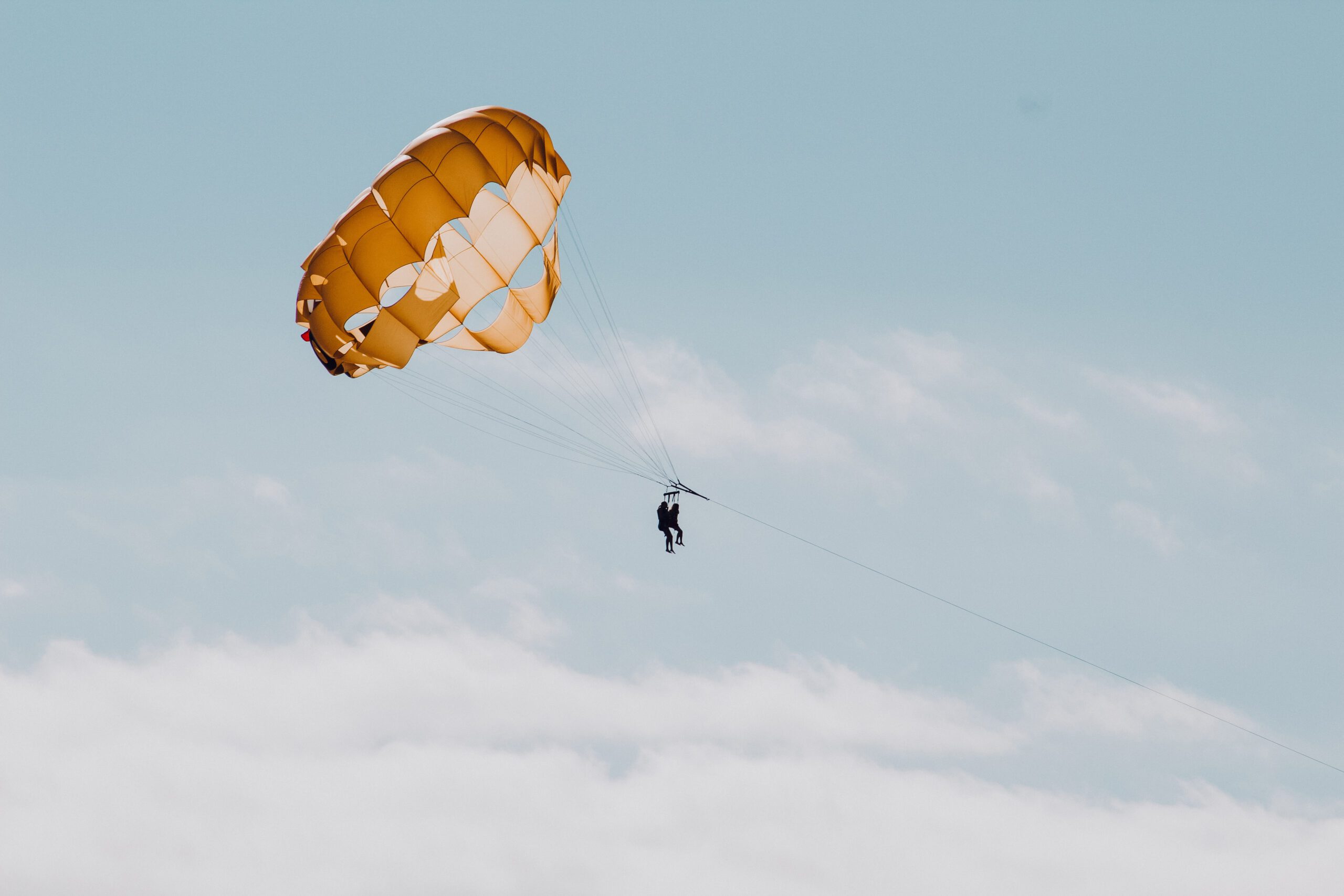 two parasailers in the sky beneath an orange parachute