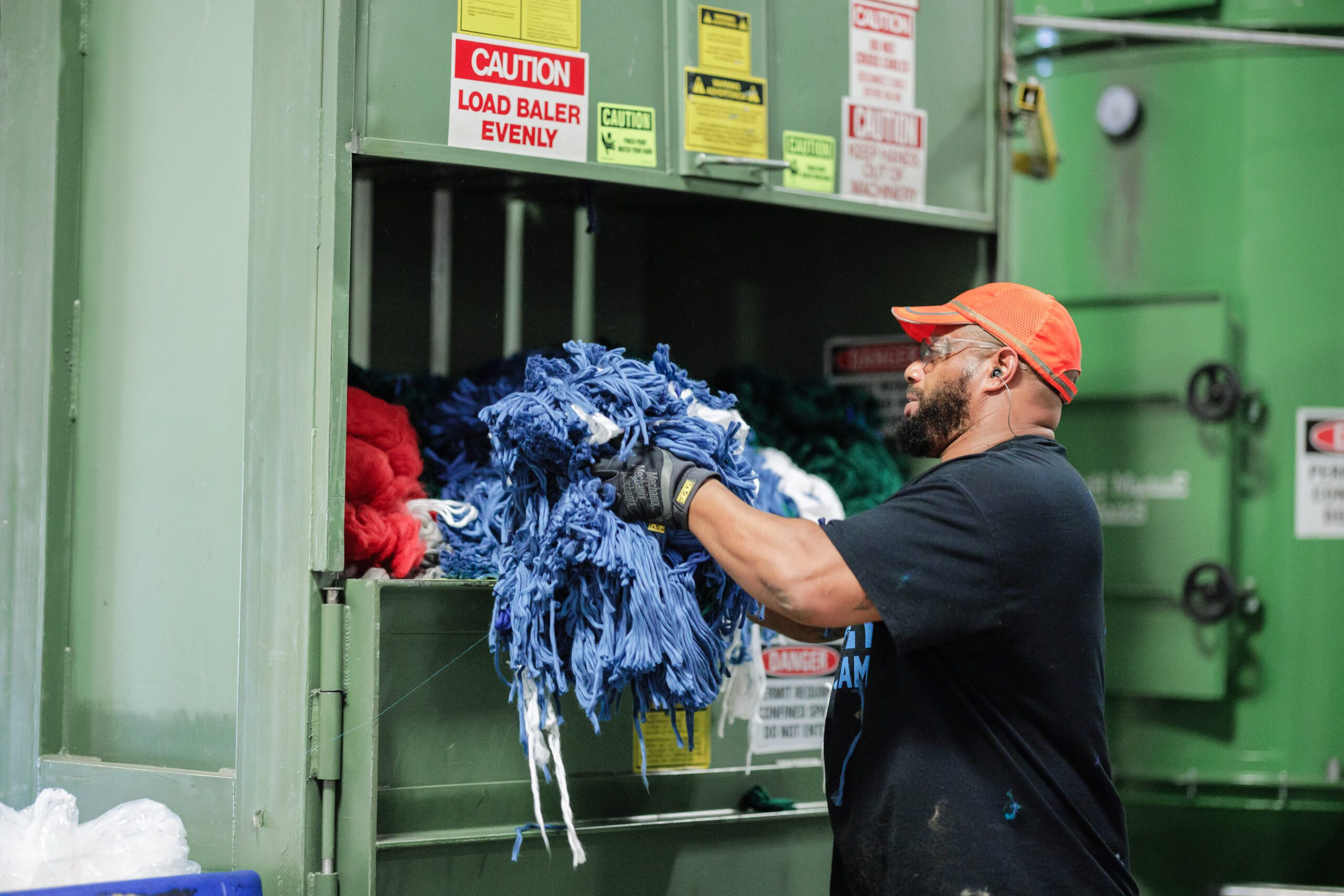 man placing a bundle of fabric into a baler