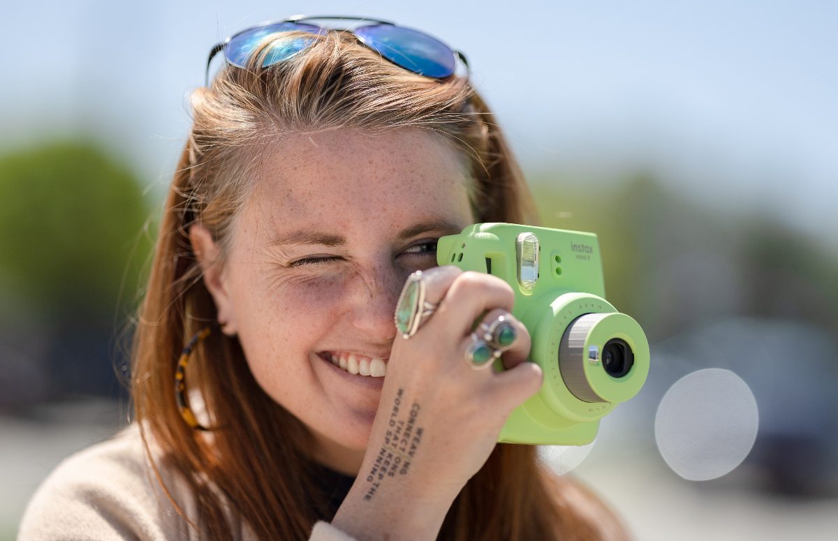 woman smiling behind bright green polaroid camera