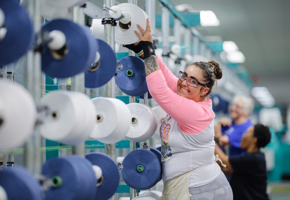 A woman puts a spool of thread on a machine