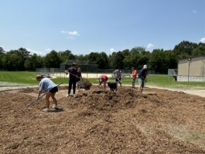 Group of men and women shovel mulch next to a baseball field